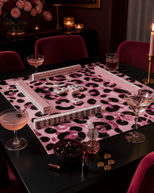 Pink leopard-print mahjong mat set for play on a dark table in a glamorous candlelit room.