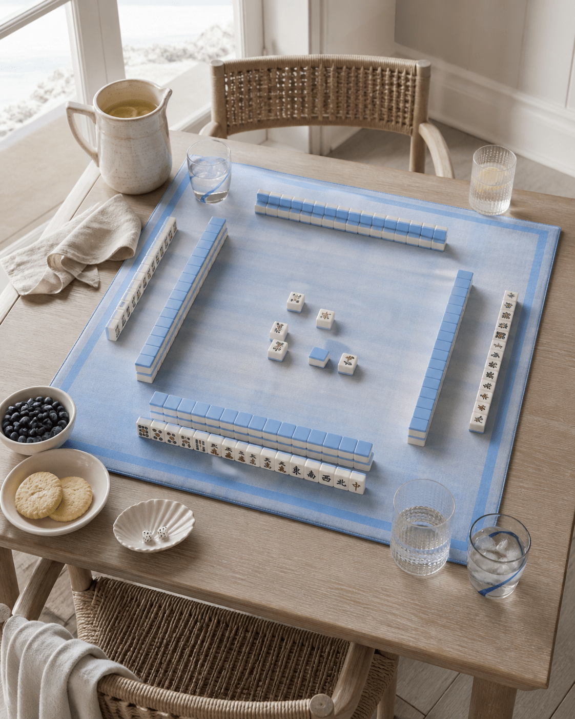 Blue plaid mahjong mat set for play with tiles and racks on a light wood dining table.