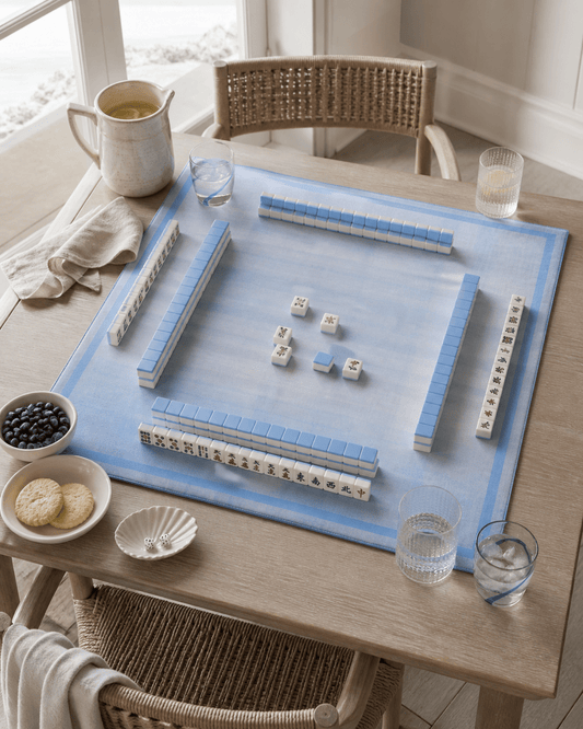 Blue plaid mahjong mat set for play with tiles and racks on a light wood dining table.
