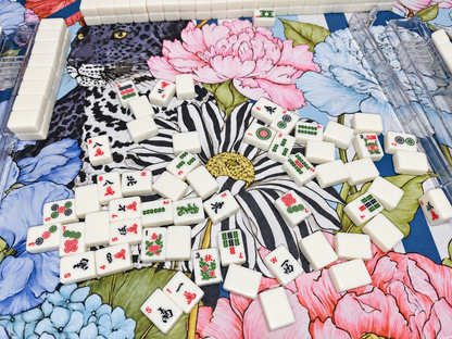 Close-up of American mahjong tiles and clear acrylic racks on a mat featuring a black leopard, colorful flowers, and a navy geometric border.