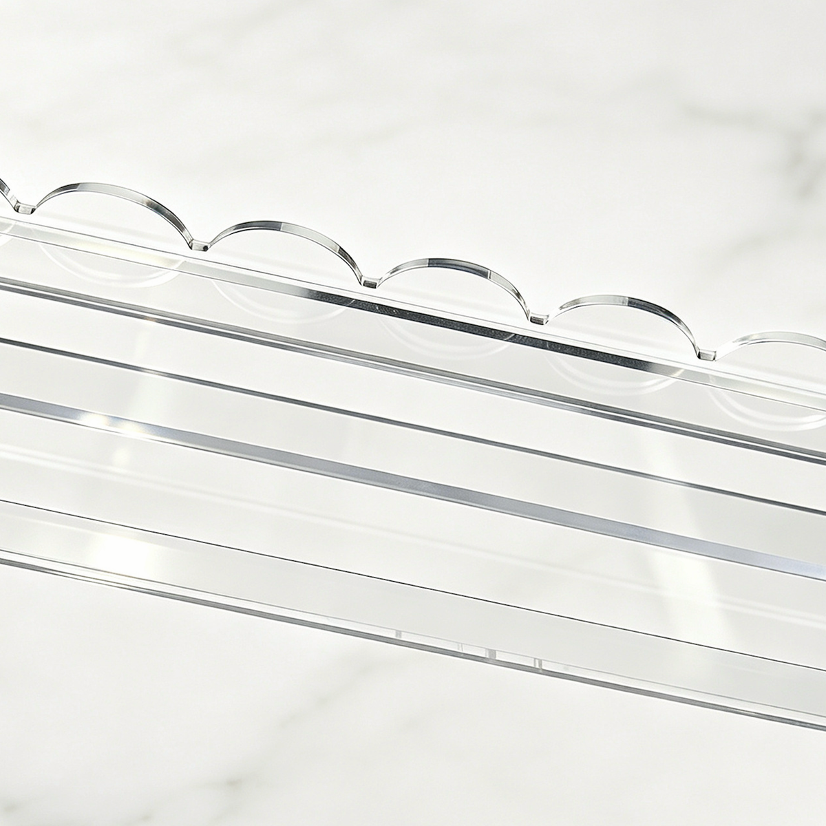Detail of the scalloped edge and straight tile ledge on a clear mahjong rack against a warm white background.