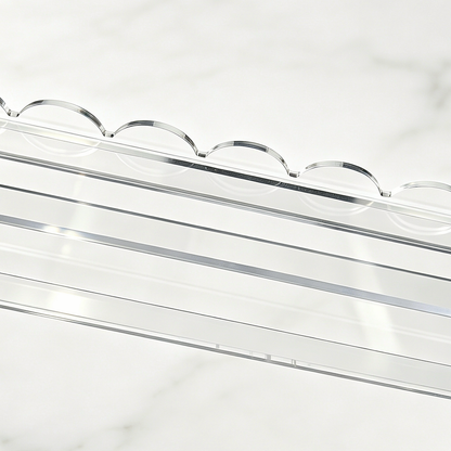 Detail of the scalloped edge and straight tile ledge on a clear mahjong rack against a warm white background.