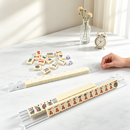 Clear mahjong rack holding tiles on a sunlit table, with a hand using the separate scalloped pusher.