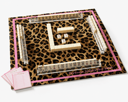 Leopard-print mahjong mat with a pink border displayed with mahjong tiles, clear racks, dice, and scorecards.