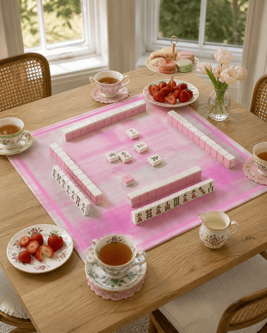 Pink plaid mahjong mat set for play on a light wood table with tea, strawberries, and flowers.