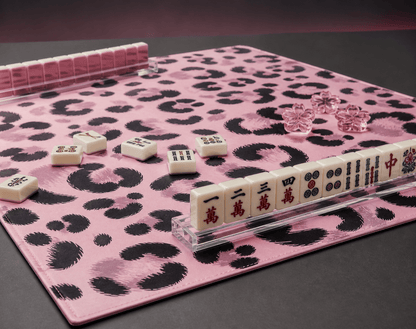 Pink and black leopard-print mahjong mat arranged with tiles and clear racks against a dark background.