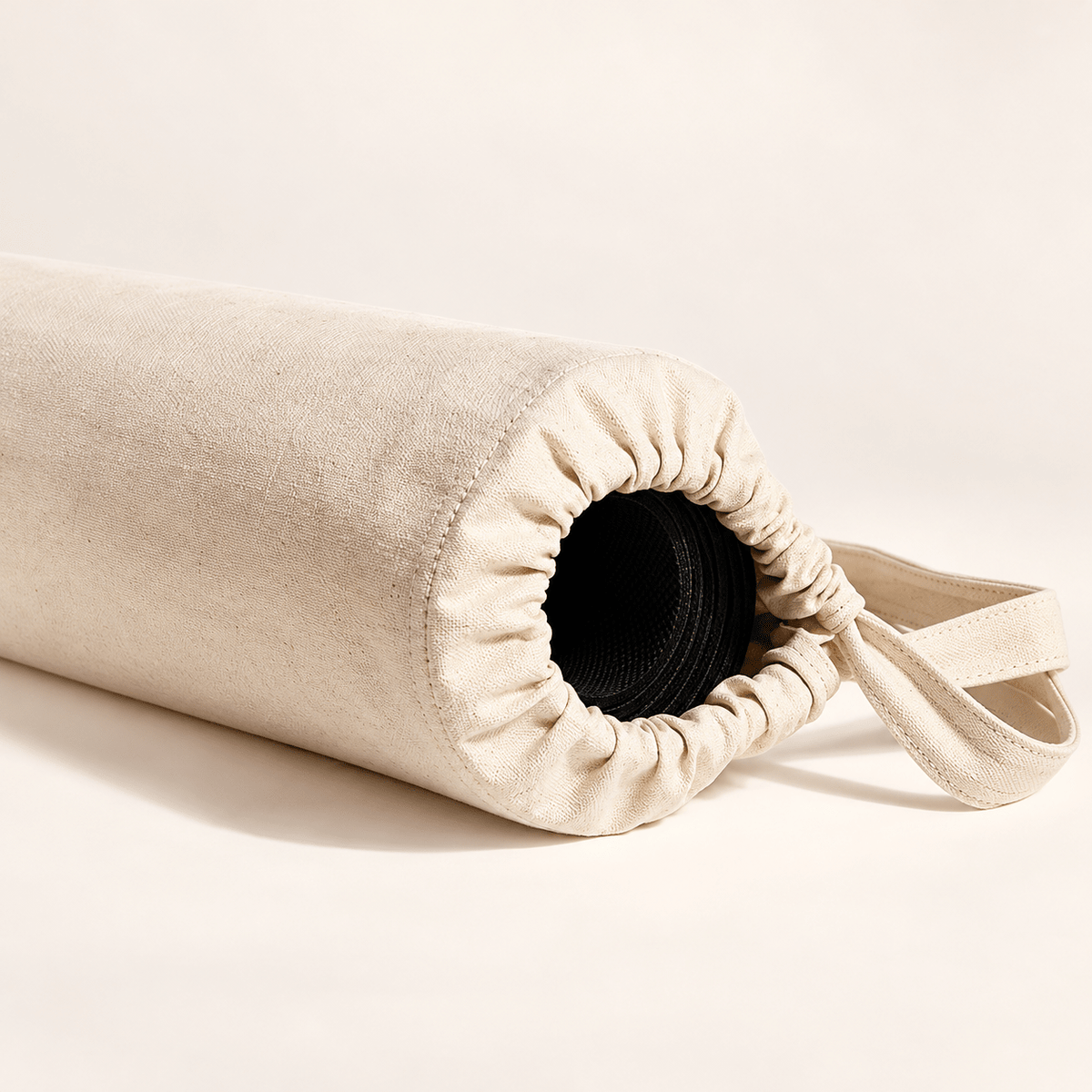 Close-up of the gathered drawstring opening of a natural canvas storage bag holding a rolled mat.